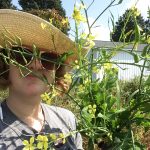 Ava Garrison stands outside on a sunny day, holding a stalk of wild radish that is partially obscuring her face.