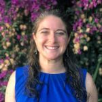 Head shot portrait of Jacqueline Gerson, standing against a background of purple flowers.