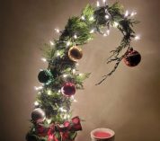 A Dr. Seuss-style evergreen arrangement is adorned with glass bulbs and lit with white string lights in a darkened room.