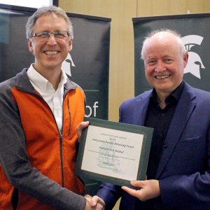 Nick Haddad stands with MSU College of Natural Science Dean Phillip Duxbury, holding the certificate for his junior faculty mentoring award honor.