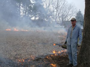 Stu Bassett pauses to pose for a picture during a prescribed burn in the pocket prairie in the Kellogg Bird Sanctuary's birds of prey area.