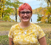 Erica Bradshaw stands outside on an autumn day with colorful trees and a lake in the background.