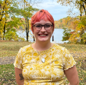 Erica Bradshaw stands outside on an autumn day with colorful trees and a lake in the background.
