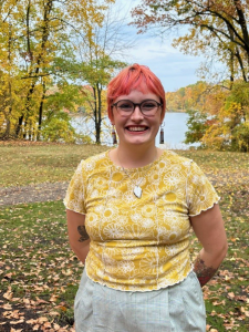 Erica Bradshaw stands outside on an autumn day with colorful trees and a lake in the background.