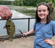 A young girl smiles while an adult holds a fish that she caught in Wintergreen Lake.
