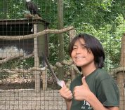 Student Cassius Caldwell, holds an eagle feather and gives a thumbs-up in front of the eagle enclosure at the W.K. Kellogg Bird Sanctuary.