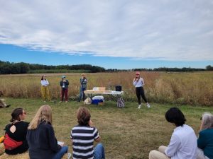 Researchers present to a group of people sitting in a half-circle on bales of straw at the KBS Long-term Ecological Research program site.