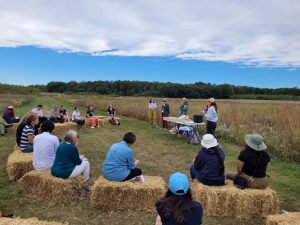 People sit in a half-circle on bales of straw listening to a presentation at the KBS Long-term Ecological Research program site.
