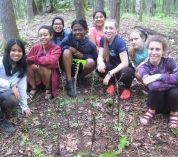 A group of participants in a past GALS program sit in a semicircle on the forest floor.