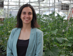 Hristina smiles in front of a green plants in a greenhouse
