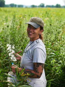 Lindsey Kemmerling stands among tall plants with narrow green leaves, taking notes.