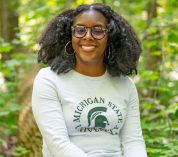 Portrait of Dr. Asia Dowtin, seated in a forested area with trees and shrubs in the background.