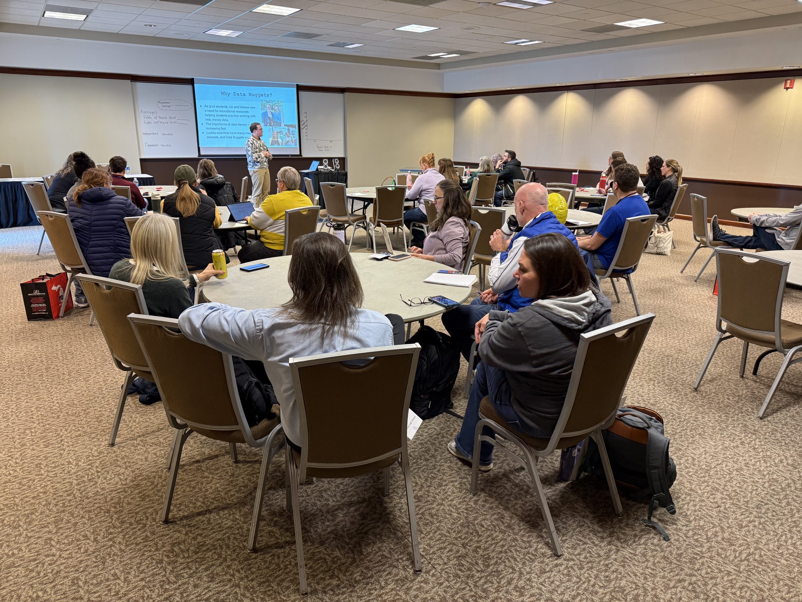 Data Nuggets Fellow Samson Stynen speaks to a room full of educators seated at round tables.