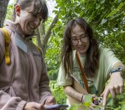 Two BioBlitz participants smile while pointing at a plant.