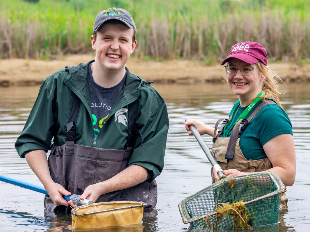 Ph.D. student Peter Martin (left) and Post Doctoral Research Associate Rosemary Martin of the Shah Lab pose for a portrait while surveying for aquatic species in the experimental pond lab at KBS.
