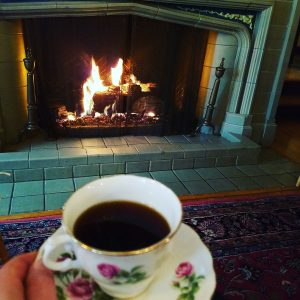 A person holds a cup of tea in an ornate teacup in front of the fireplace in the Manor House living room.