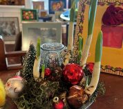 A winter arrangement featuring narcissus bulbs, a miniature evergreen tree, and tree ornaments, sits on a table.