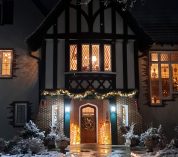 Nighttime view of the W.K. Kellogg Manor House, with the front door adorned with festive lights and the interior rooms glowing with light.