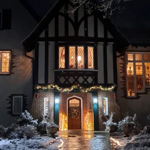 Nighttime view of the W.K. Kellogg Manor House, with the front door adorned with festive lights and the interior rooms glowing with light.
