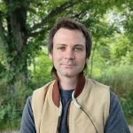 Tyler Linderoth stands in front of a forested area.