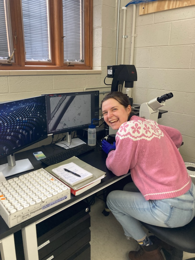 Rachel Drobnak smiles while sitting at a computer desk in a lab at the W.K. Kellogg Biological Station.