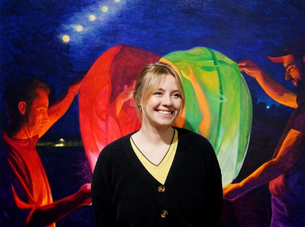 Artist Ellen VanderMyde stands smiling against a green and red background.